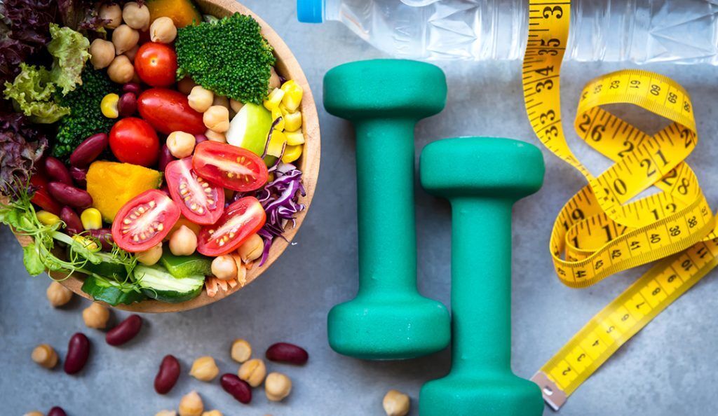 a healthy salad with weights and a tape measure to illustrate healthy lifestyle