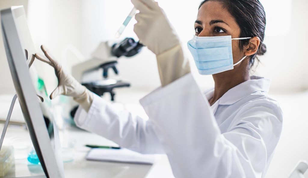 a female scientist wearing a lab coat and mask analyzes samples
