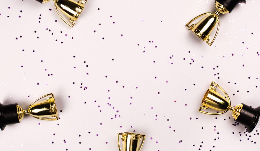 five trophies against a pink background with confetti