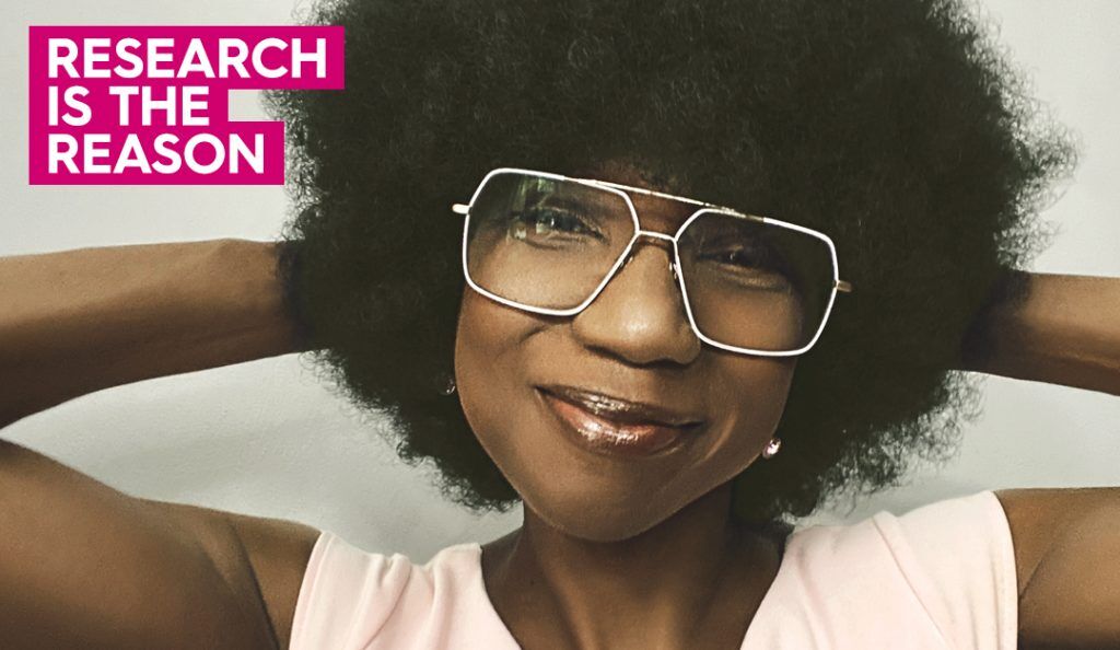 portrait of suzette simon wearing an afro wig and smiling at the camera in a pink top