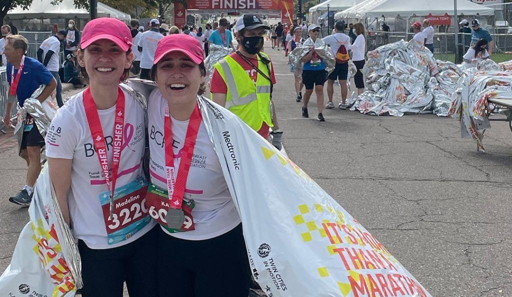 madeline and her sister at the finish line of the twin cities marathon wearing medals and BCRF shirts