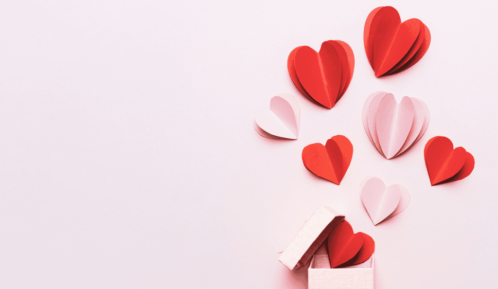 cut outs of red and pink paper hearts against a light pink background||