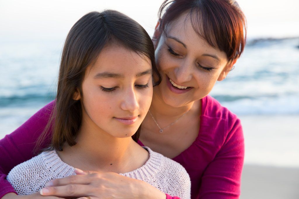 a latin/hispanic mom embraces her daughter on the beach