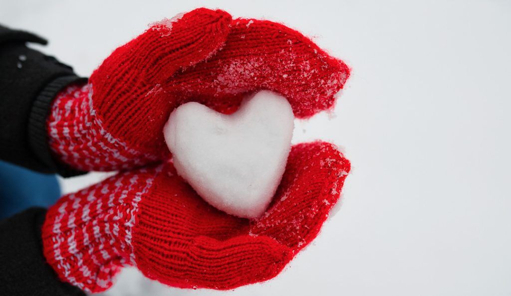 person wearing red mittens holding a snowball shaped like a heart