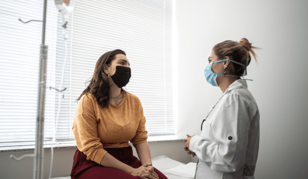 a young woman talks with her doctor who stands in a lab coat with her hair tied back