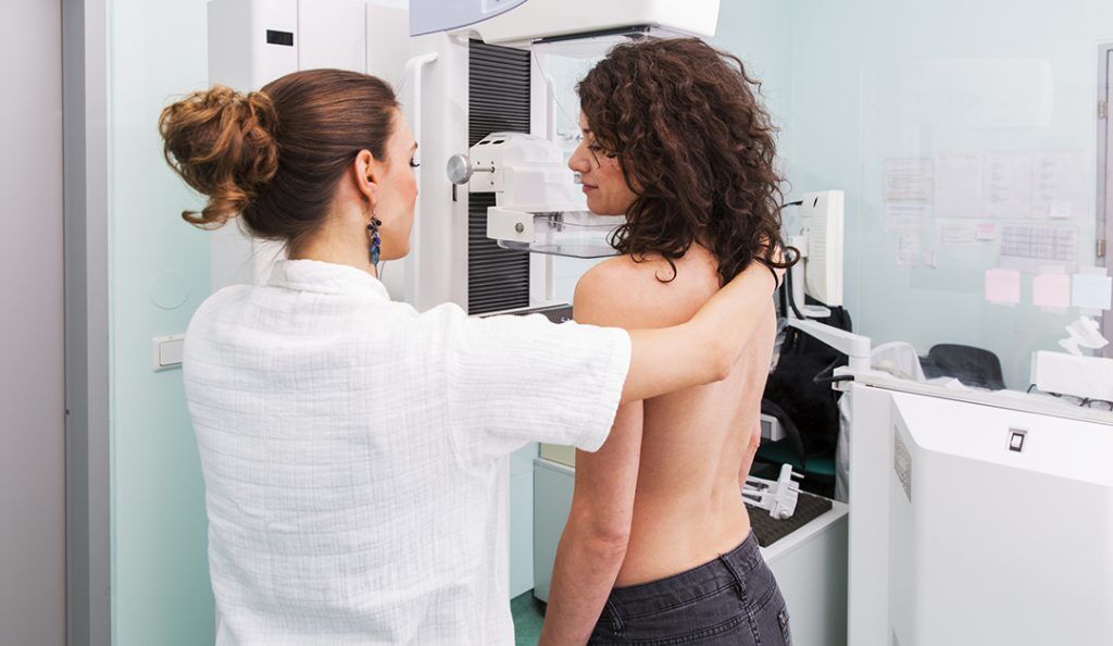 a young women stands in front of a mammogram machine with a technician