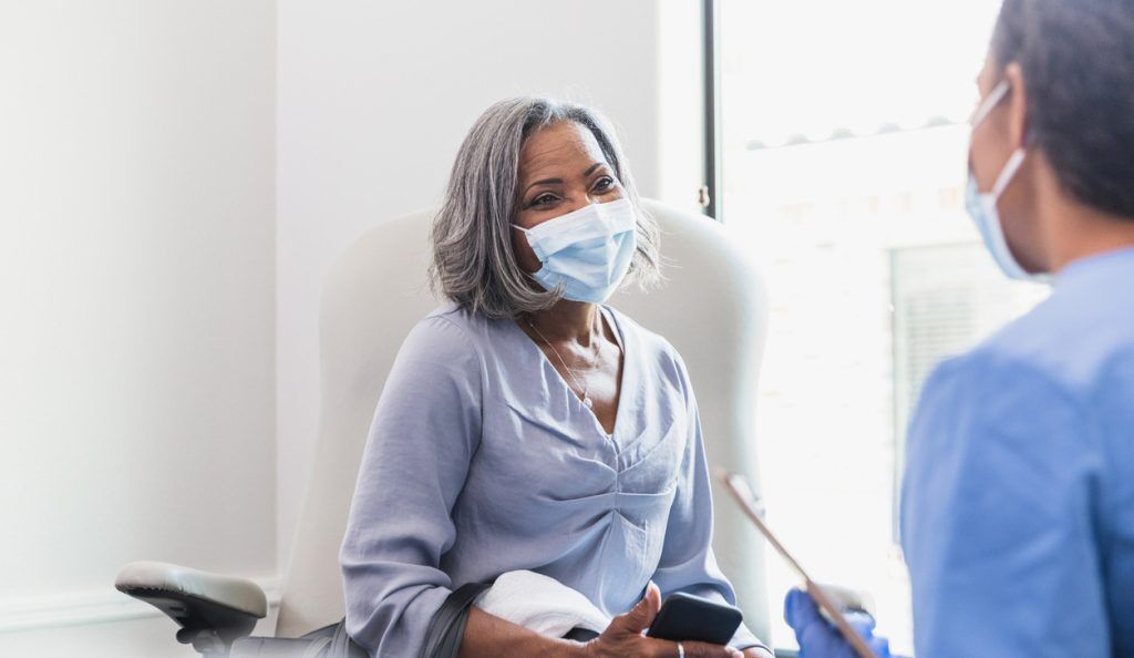 woman wearing face mask consults with her doctor at an appointment