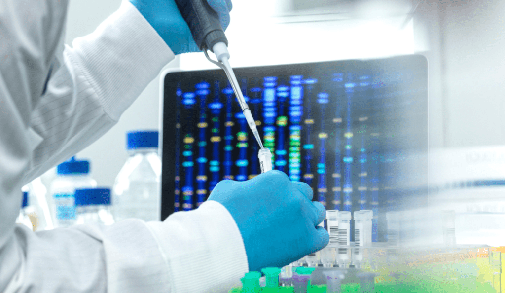 a researcher prepares a sample with a computer behind him showing gene sequencing results