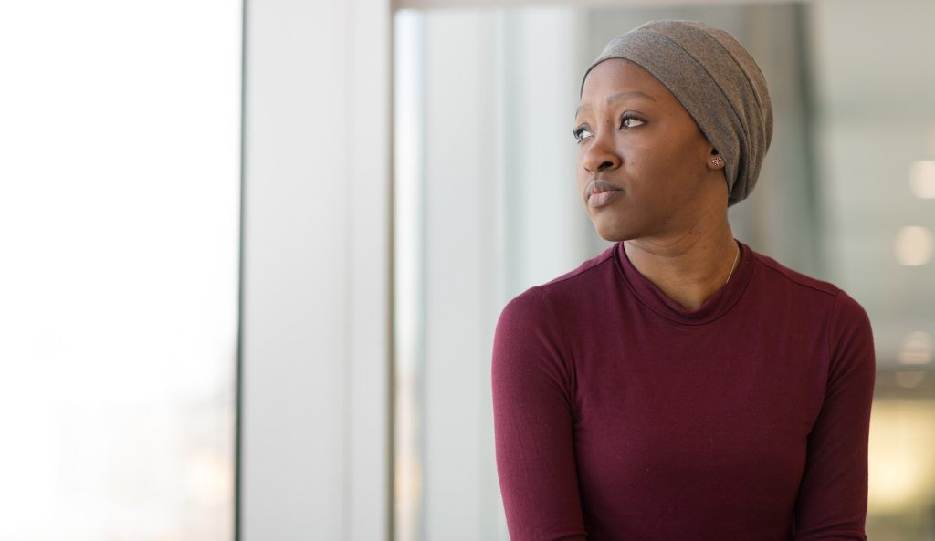 african american cancer patient looking out window wearing scarf on head