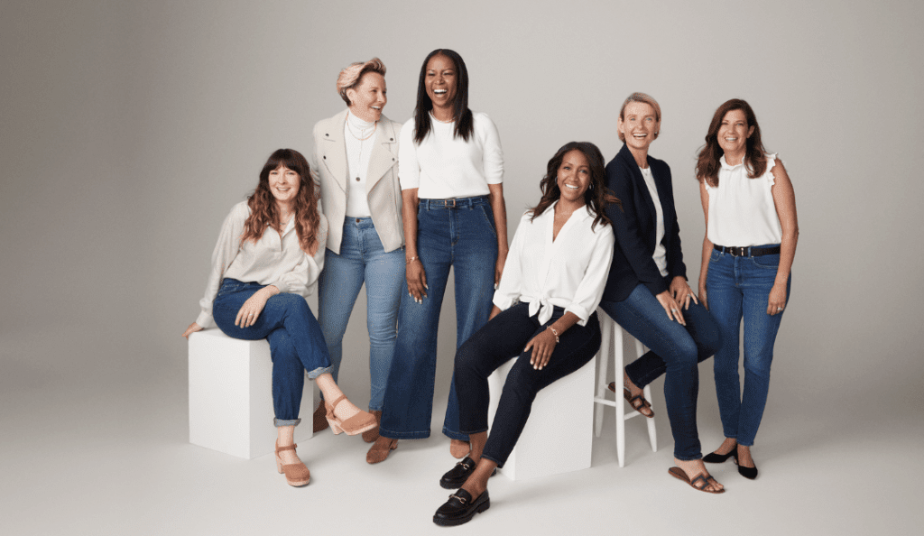 Lizanne Kindler poses with five breast cancer thrivers against a simple white background; the diverse group of women all wear jeans and white tops