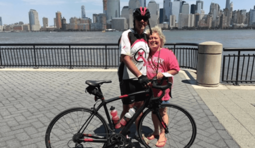 al and terry pose with al's bike with a view of the new york city skyline in the background