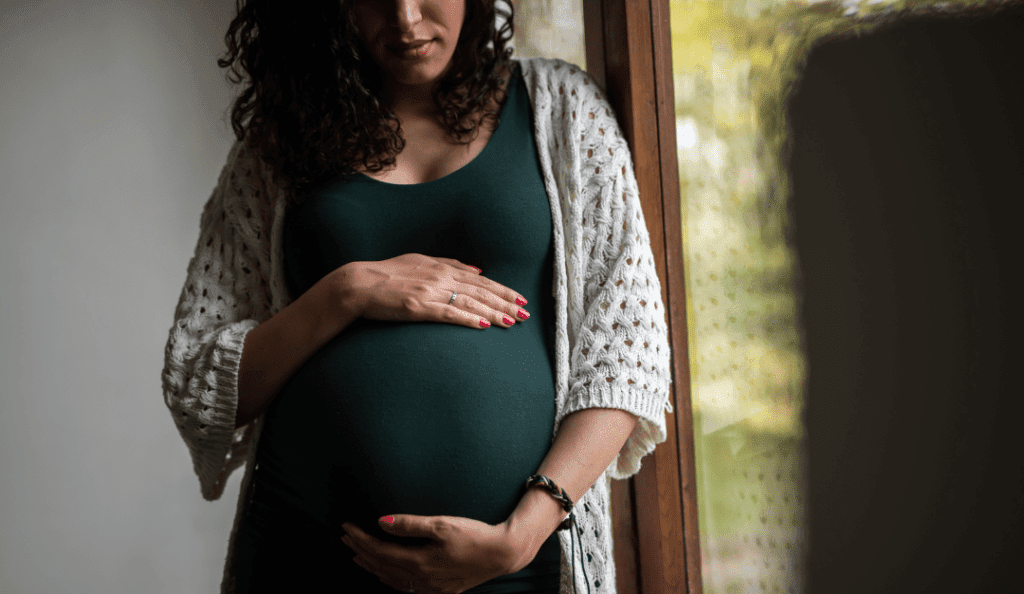 a pregnant woman holds her belly wearing a dark green shirt and cardigan