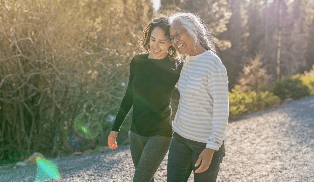 an older woman walks with her adult daughter outside in the sun