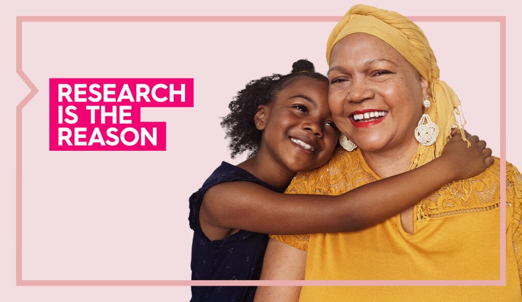 Maria wears a yellow shirt and smiles at the camera while her granddaughter hugs her against a light pink background