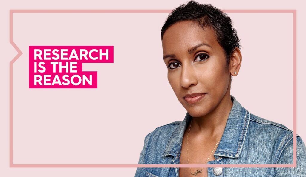Sadia wears a blue shirt and smiles at the camera against a light pink background