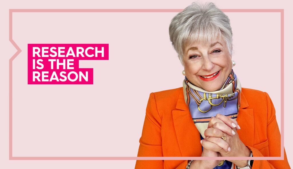 Ellen wears an orange blazer and smiles at the camera against a light pink background