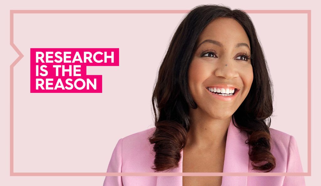 Amanda wears a pink blazer and smiles at the camera against a light pink background