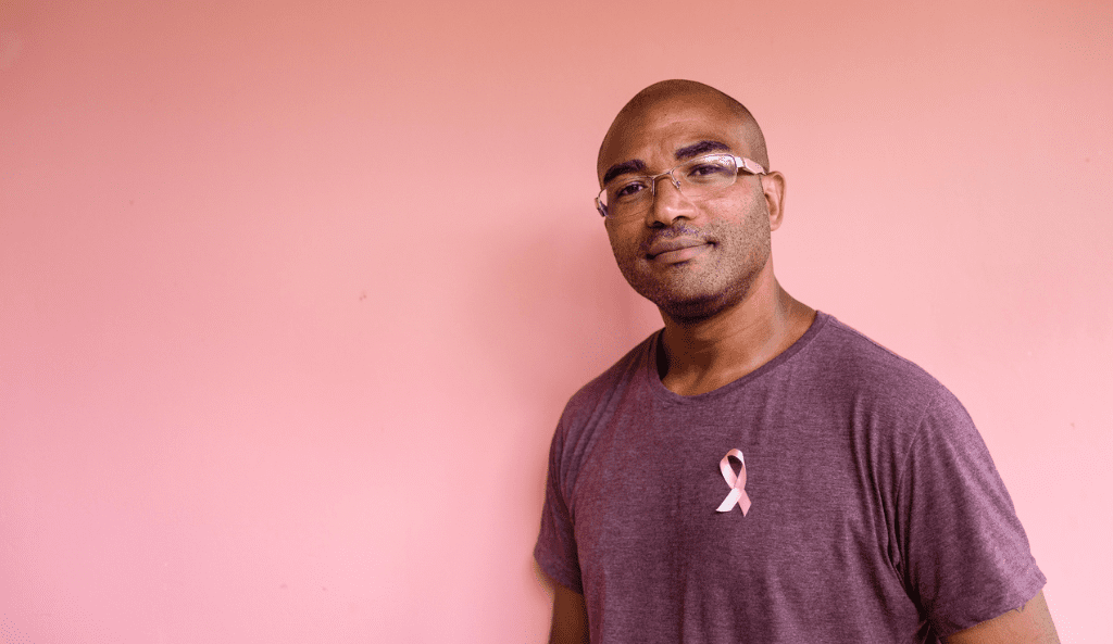 portrait of a black man wearing a maroon shirt with a pink ribbon on his chest, evokes male breast cancer