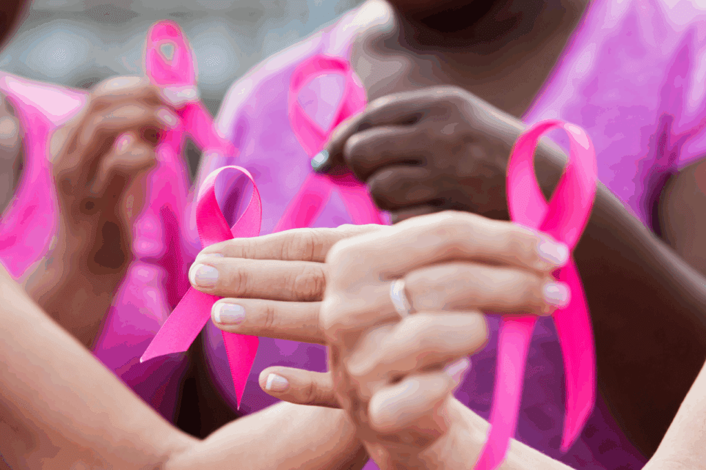 Women gathering in a line holding a pink ribbon for breast cancer awareness in their hands