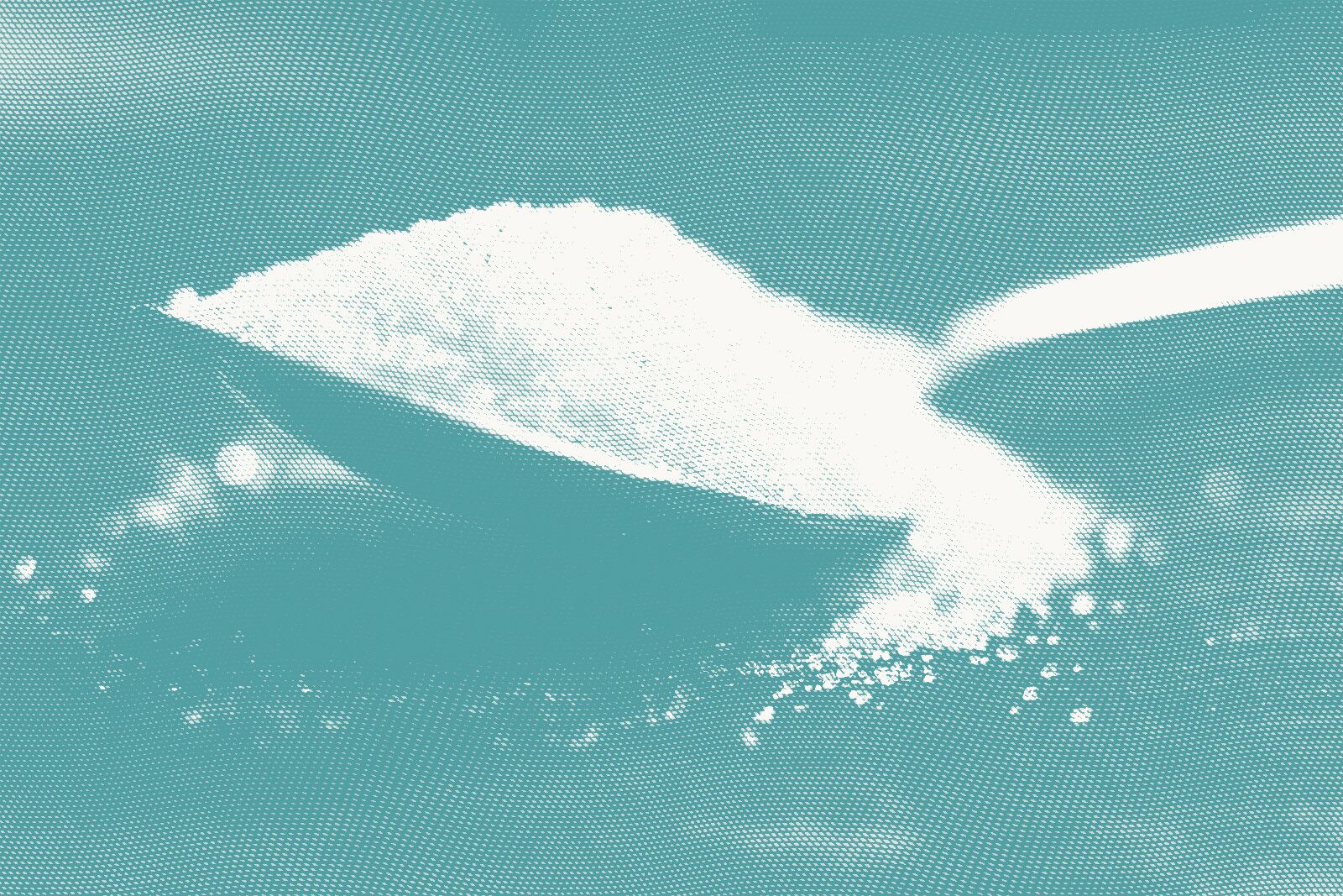 a spoon heaped with granulated white sugar rests on a table