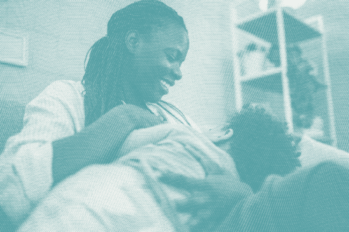 a woman breastfeeds her son, he's facing away from the camera and she's looking down smiling at him