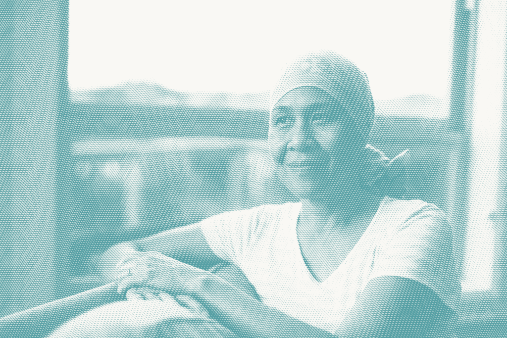 an older woman sits next to a window. she's wearing a headscarf as she's lost her hair after chemotherapy for breast cancer