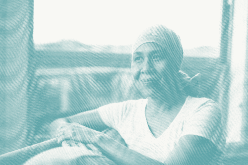 an older woman sits next to a window. she's wearing a headscarf as she's lost her hair after chemotherapy for breast cancer