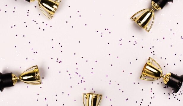 five trophies against a pink background with confetti